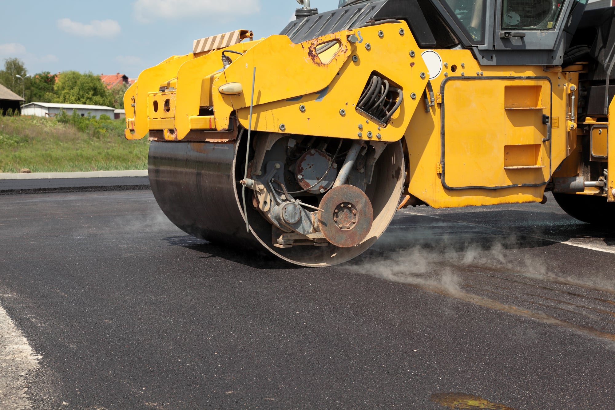 Close-up of a steel-drum roller compacting hot asphalt during a paving pass